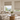 Two textured beige Roman blinds lowered to different heights over sunlit living room windows.